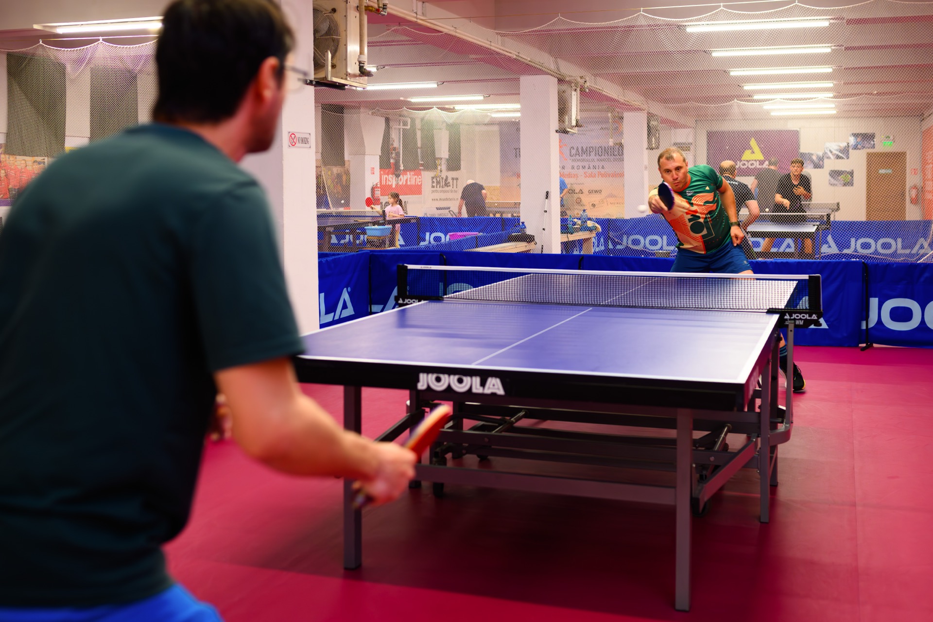 Action shot: player mid-rally with the full club hall in view